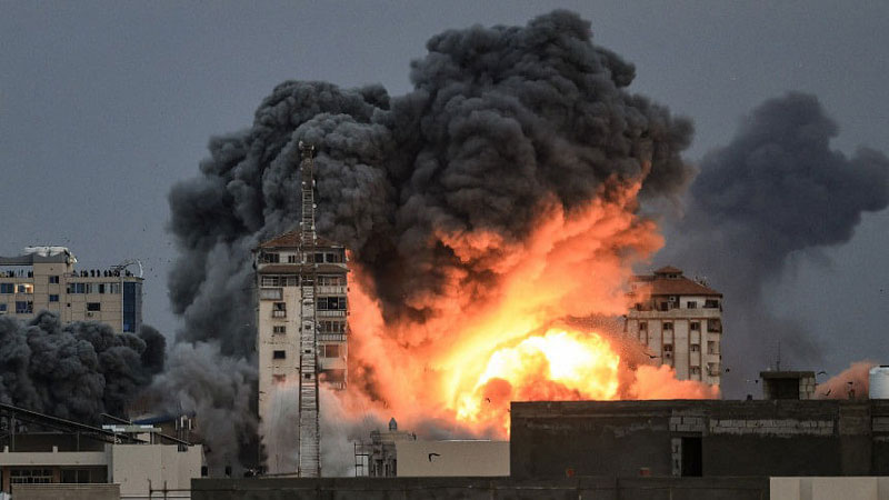 People standing on a rooftop watch as a ball of fire and smoke rises above a building in Gaza City on October 7, 2023 during an Israeli air strike that hit the Palestine Tower building. Photo: AFP